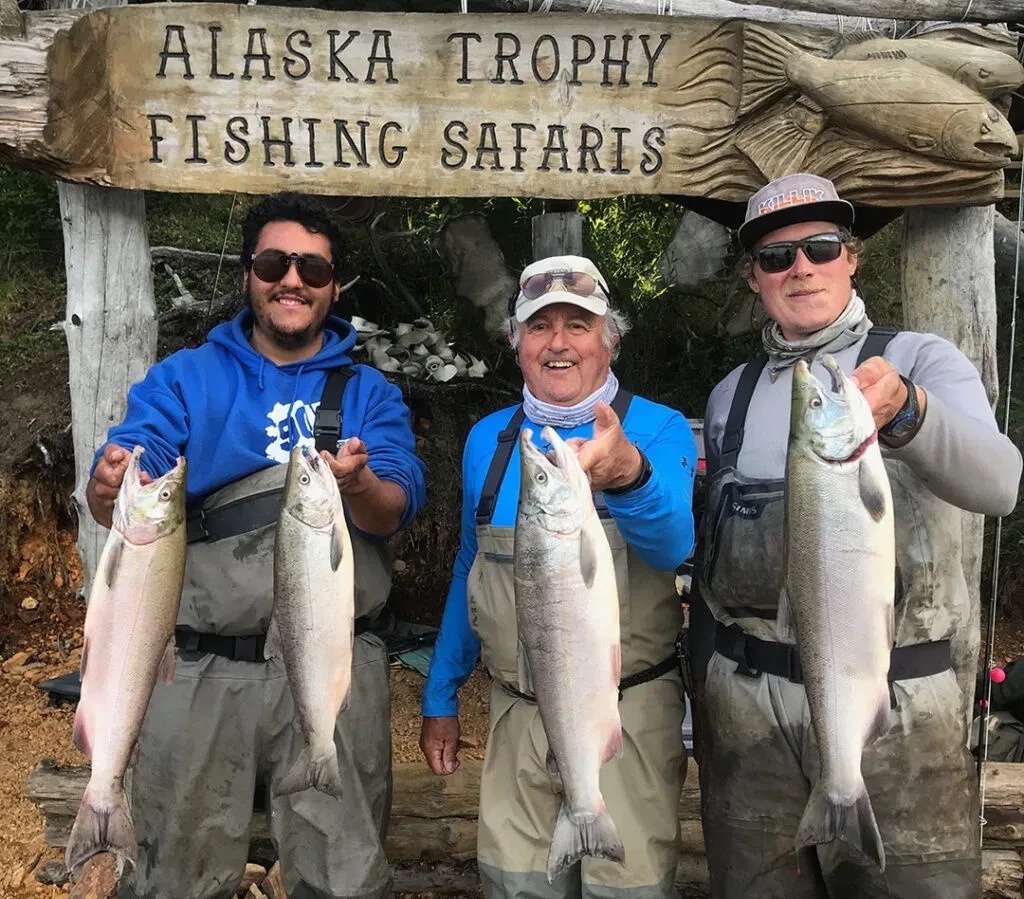 Three guests with their salmon beneath the Alaska Trophy Fishing Safaris camp sign